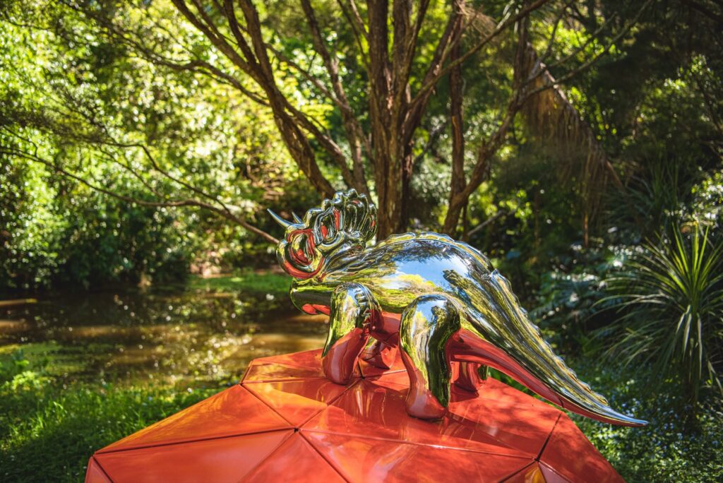 A chrome dinosaur sculpture on an orange plinth on the Brick Bay Sculpture Trail