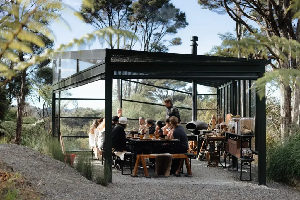Guests sharing a meal in Velskov's glass pavilion in the Waitākere Ranges forest